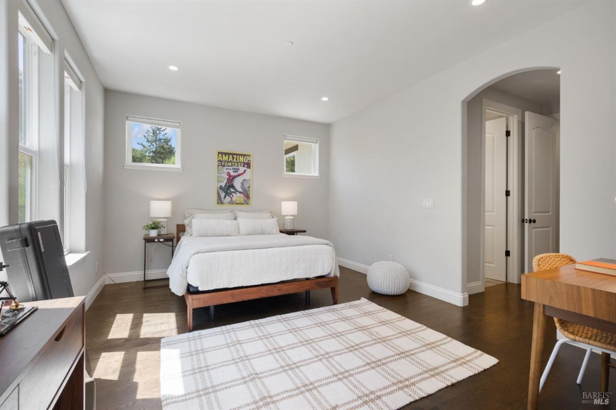 The bedroom features a bed, a desk with a chair, a rug, and two windows.