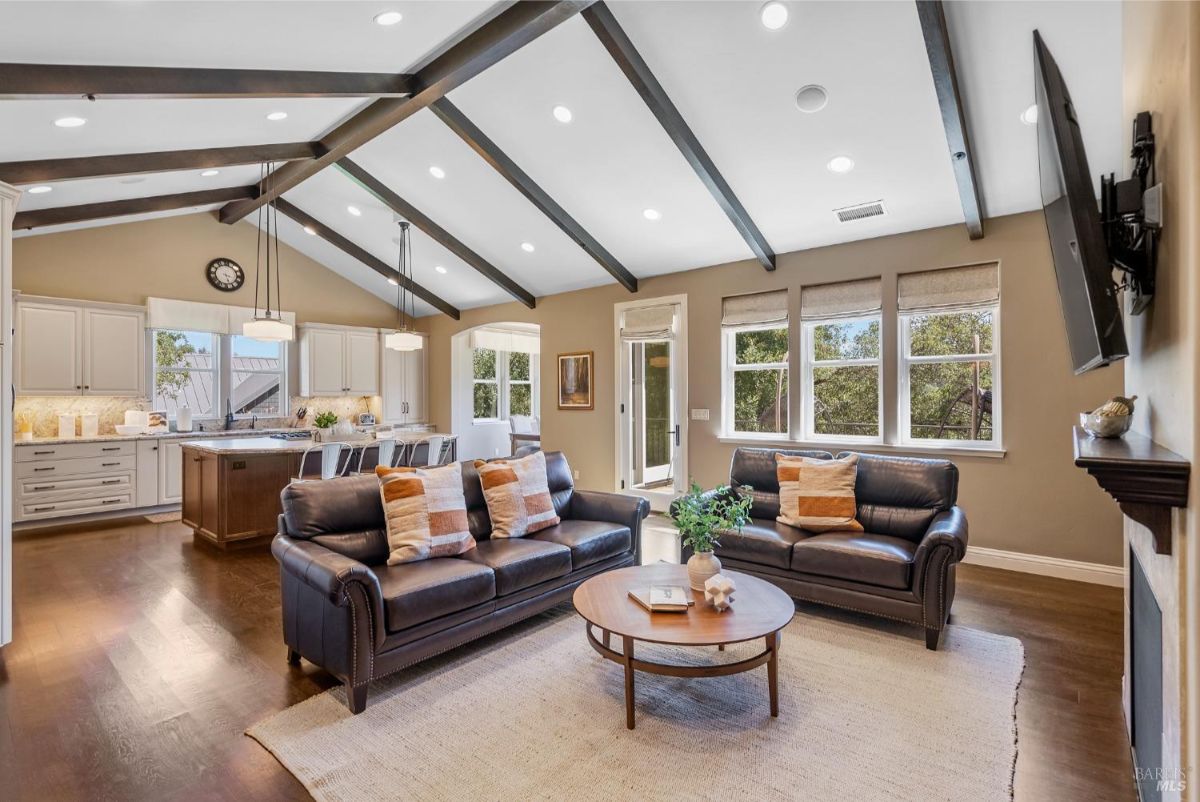 Open-concept living and dining space with a modern kitchen, exposed beams, and leather sofas.