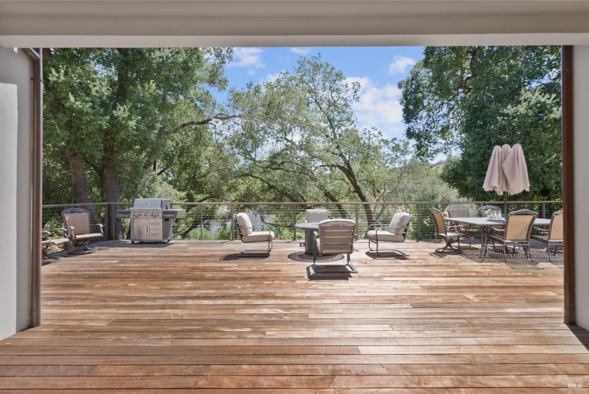 The outdoor space features a large deck with a seating area, a dining table, and a grill.