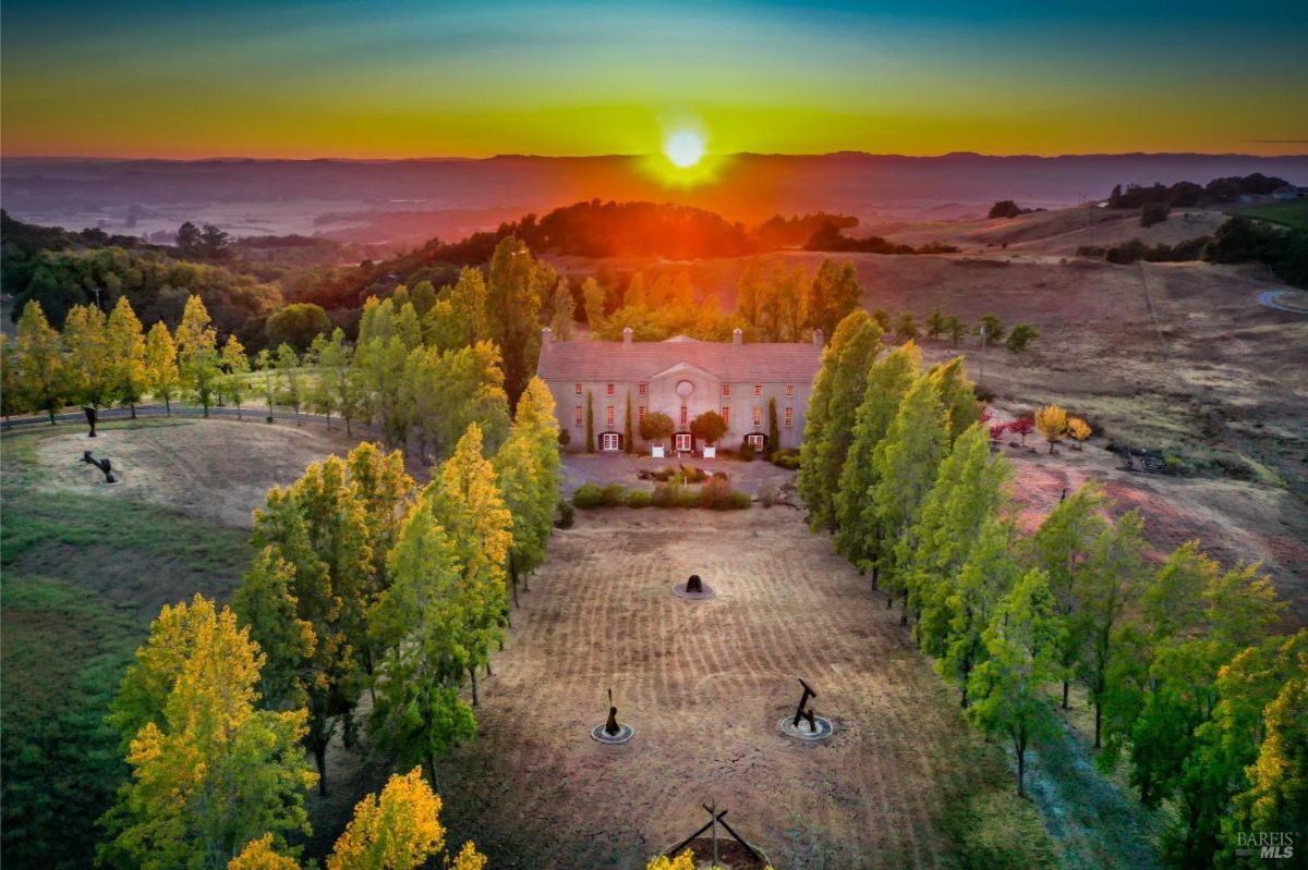 A grand estate surrounded by vibrant green trees, captured at sunset with rolling hills in the background.