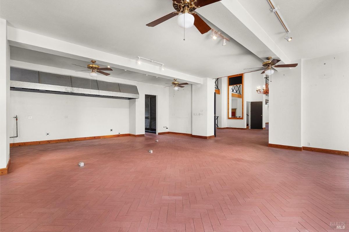 A room with ceiling fans and an industrial-style hood, adjacent to other open spaces.