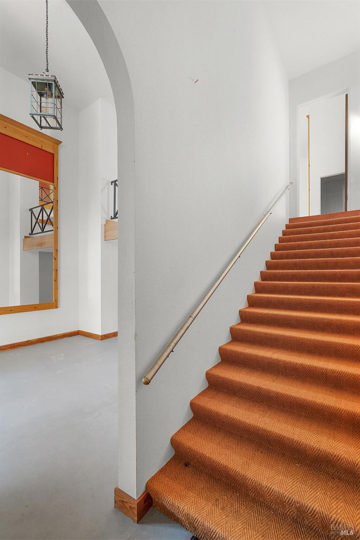 A staircase with orange carpeting and a metal handrail, leading to a bright upper floor with arched doorways.