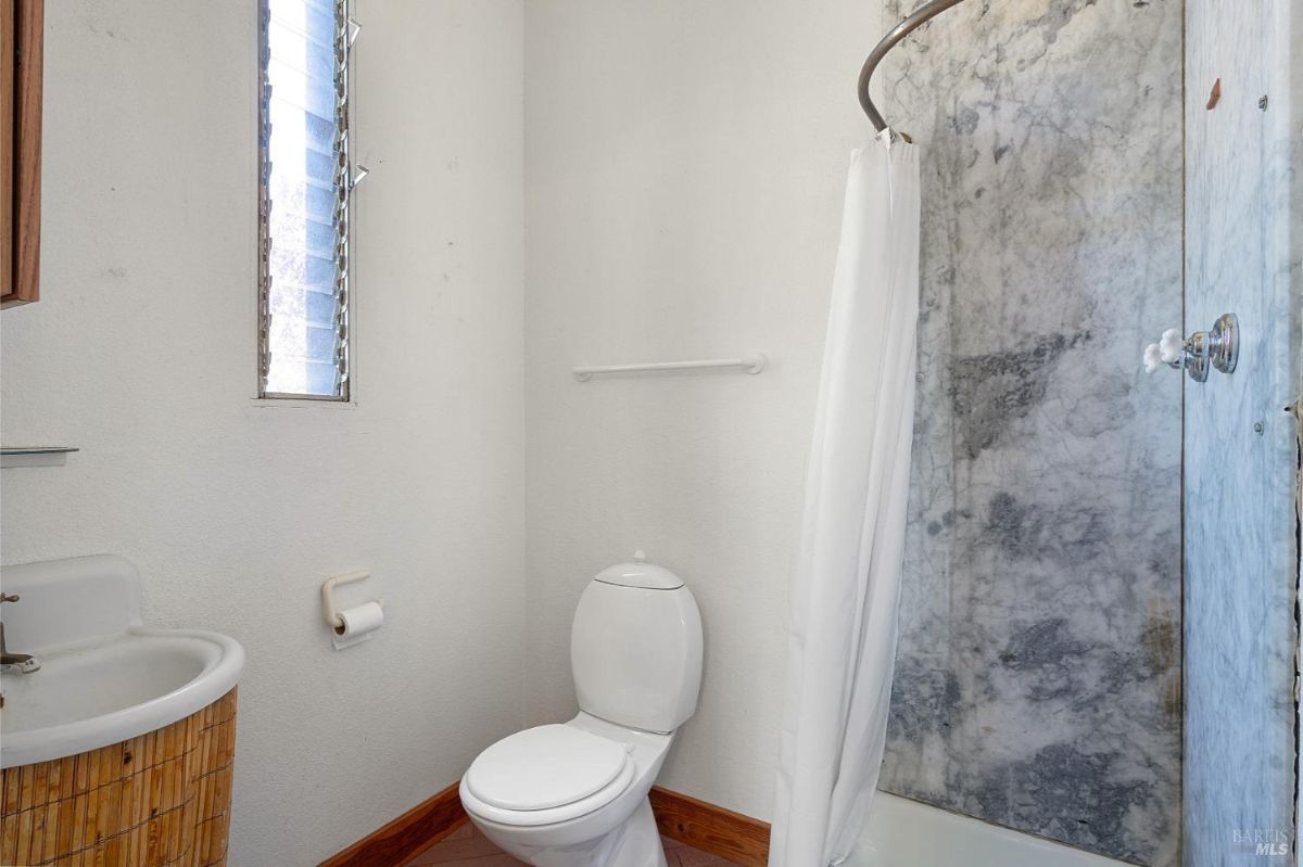 A small bathroom with a marble shower, wood sink cabinet, and a narrow frosted window.