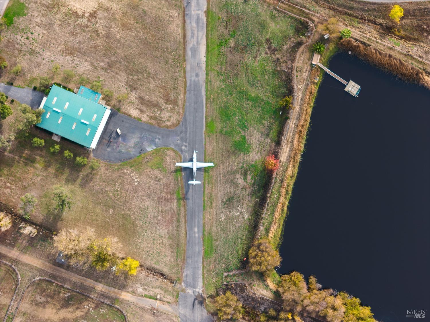 This aerial view showcases a private airstrip with a plane prepared for takeoff, adjacent to a hangar and a serene pond. The surrounding greenery and vast open space emphasize the secluded and self-sufficient nature of this property.