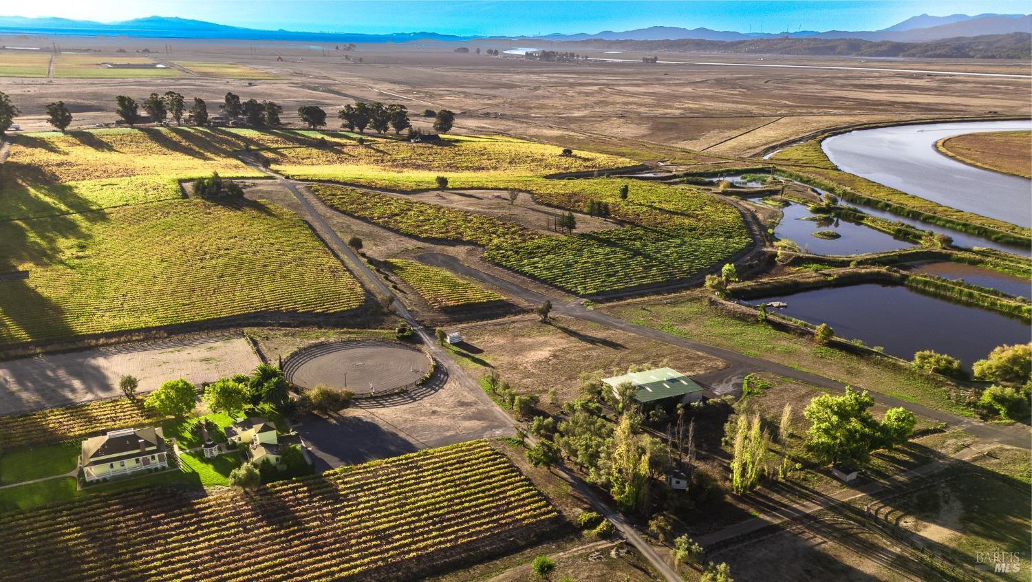 This sprawling estate, captured in an aerial view, showcases a harmonious blend of natural beauty and carefully planned amenities. Vineyards, a meandering river, and tranquil ponds create a picturesque landscape, while the presence of riding arenas and structures hint at equestrian pursuits and comfortable living. This property truly offers a serene and self-sufficient lifestyle.