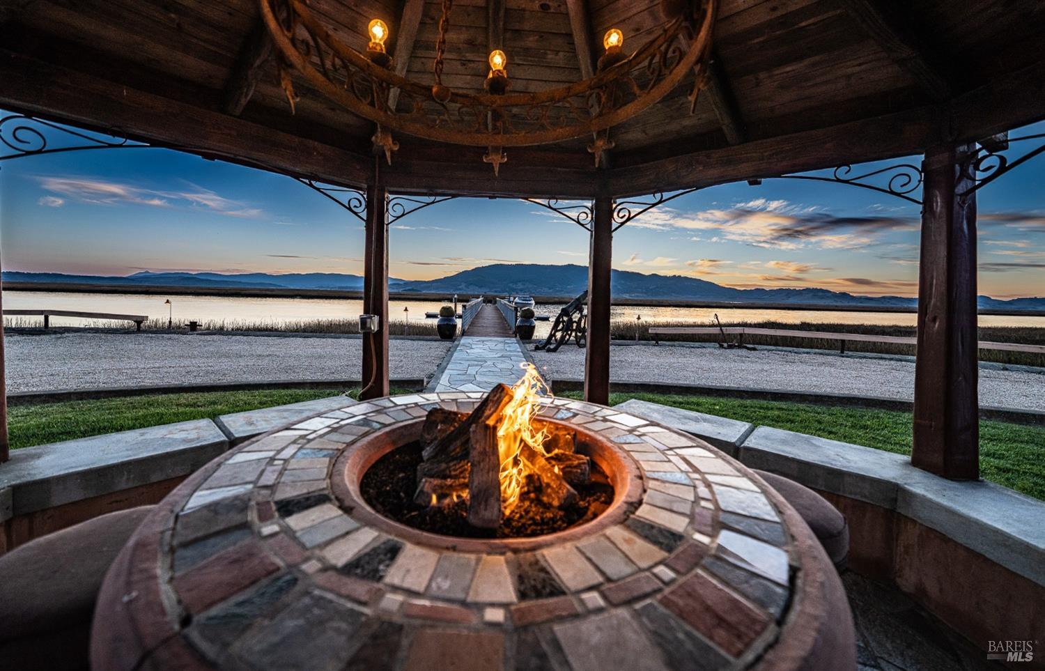 A cozy gazebo with a rustic chandelier and a built-in fire pit offers a perfect spot to enjoy a mesmerizing waterfront sunset. The crackling flames, tranquil water, and vibrant sky create an unforgettable ambiance for relaxation and connection with nature.