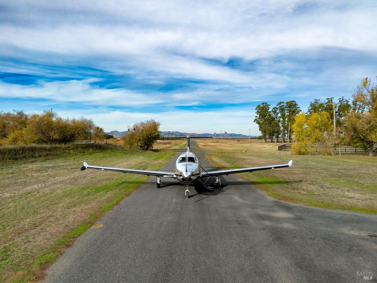 A small, single-engine plane sits on a runway, ready for takeoff. The sky is a beautiful blue with fluffy white clouds.