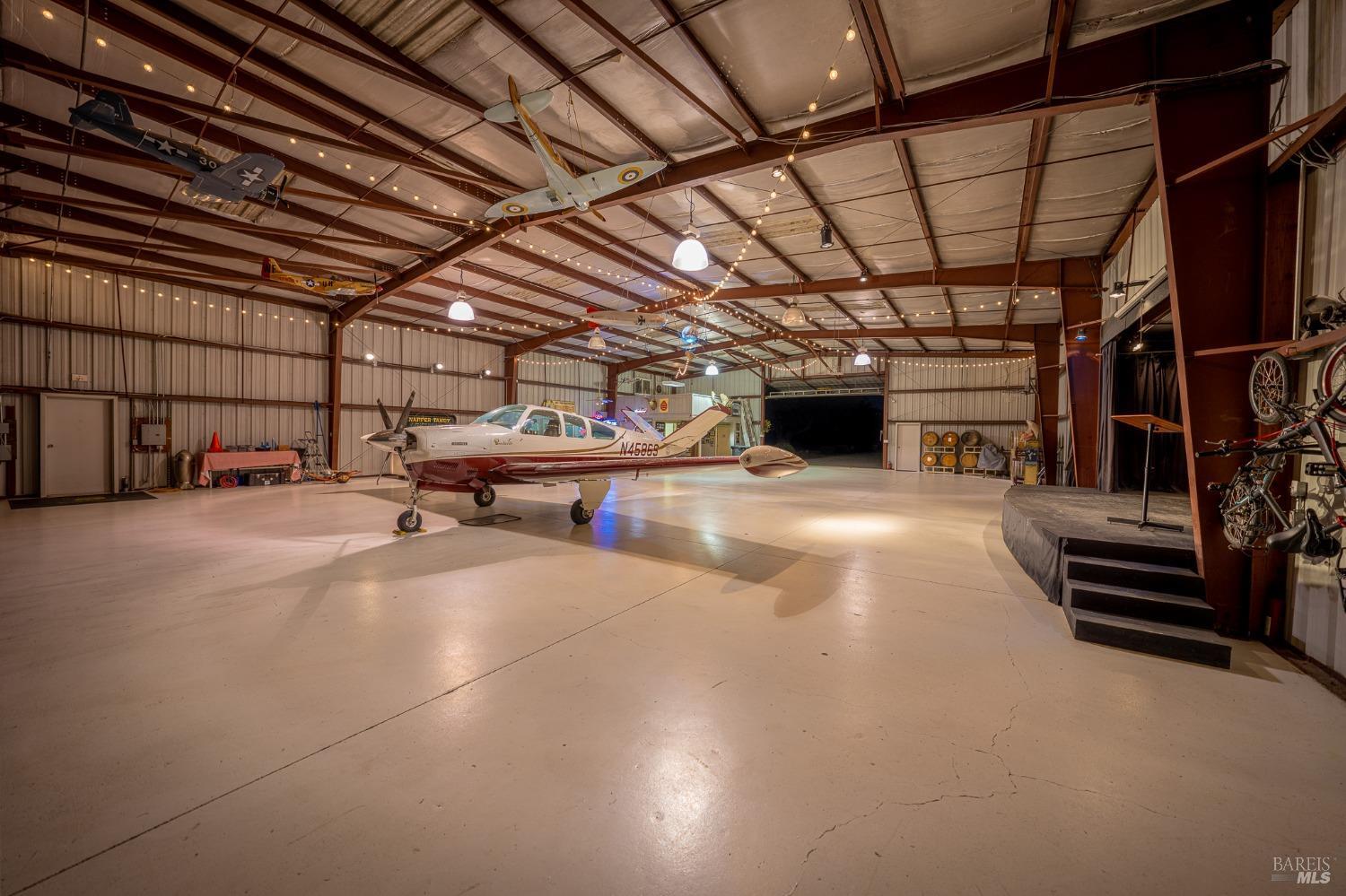 This spacious hangar, adorned with model airplanes and equipped with a stage, serves as a unique and versatile space. It comfortably houses a private plane while also offering room for gatherings and entertainment, showcasing a blend of practicality and leisure.