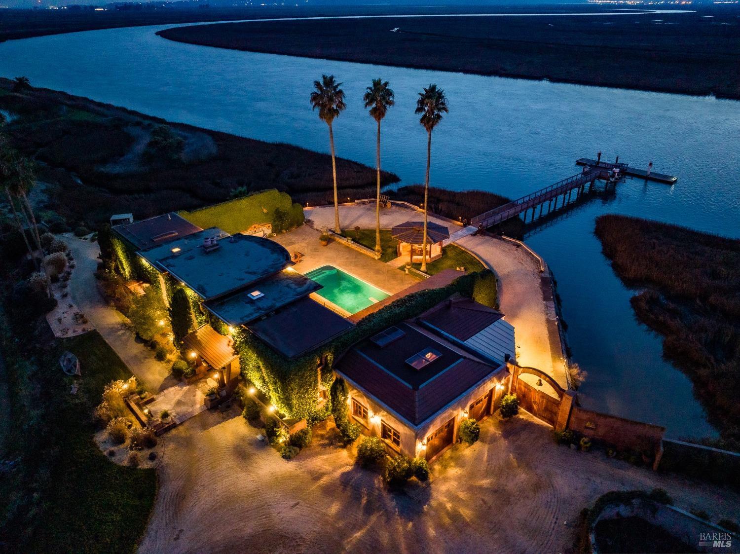 This stunning waterfront estate, bathed in the warm glow of evening lights, offers a private oasis with its own pool and dock. The surrounding lush landscape and tranquil waters create a picturesque and serene retreat.