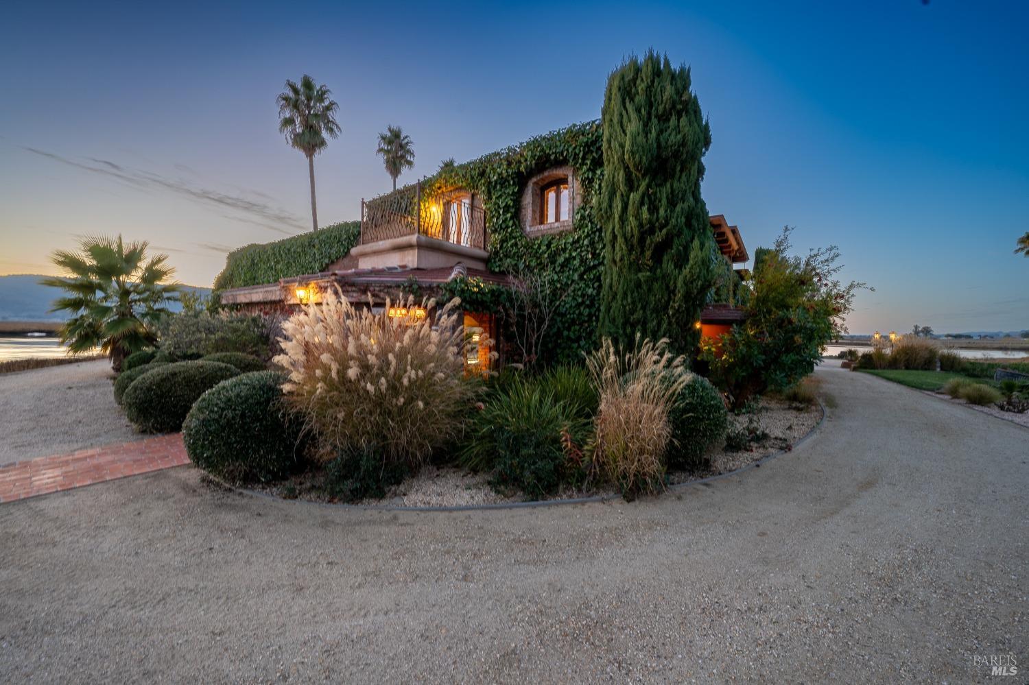 This ivy-clad home, bathed in the soft glow of dusk, exudes a romantic charm. Lush landscaping and a circular driveway add to the elegance, while a glimpse of the waterfront in the distance hints at the serene setting of this private retreat.