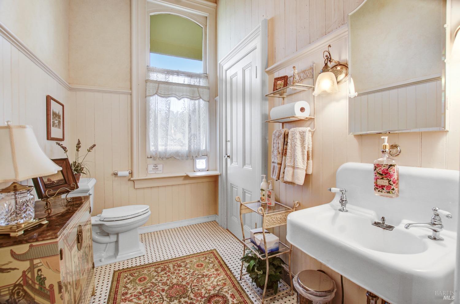 This charming bathroom blends vintage elements with modern conveniences. The room features a classic pedestal sink, beadboard wainscoting, and a decorative rug, while still offering necessary amenities for a comfortable experience.