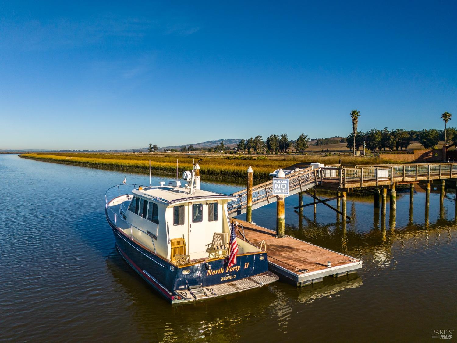 "North Forty II", a beautiful boat, is peacefully docked at a private pier with a "No Trespassing" sign, enjoying the serenity of the calm waters under a clear blue sky. The American flag flutters proudly from the stern, adding a patriotic touch to this idyllic waterfront scene.