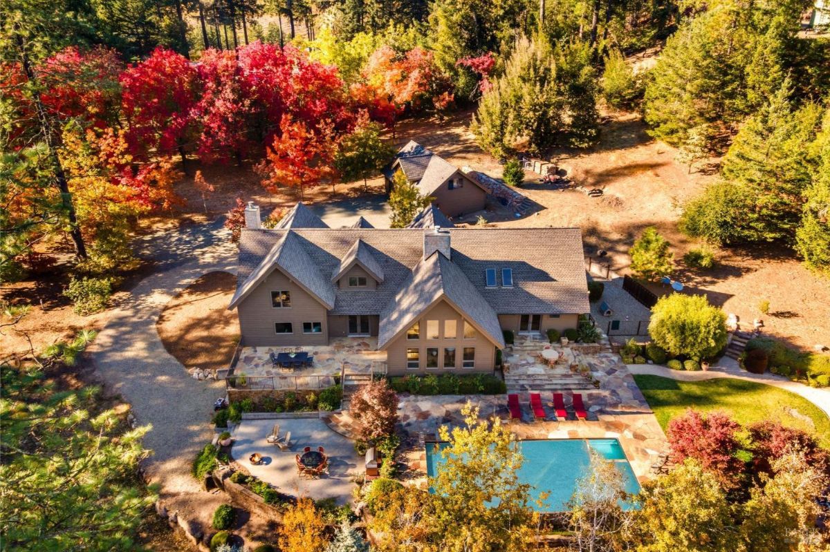 House surrounded by vibrant autumn-colored trees with a pool in the foreground.