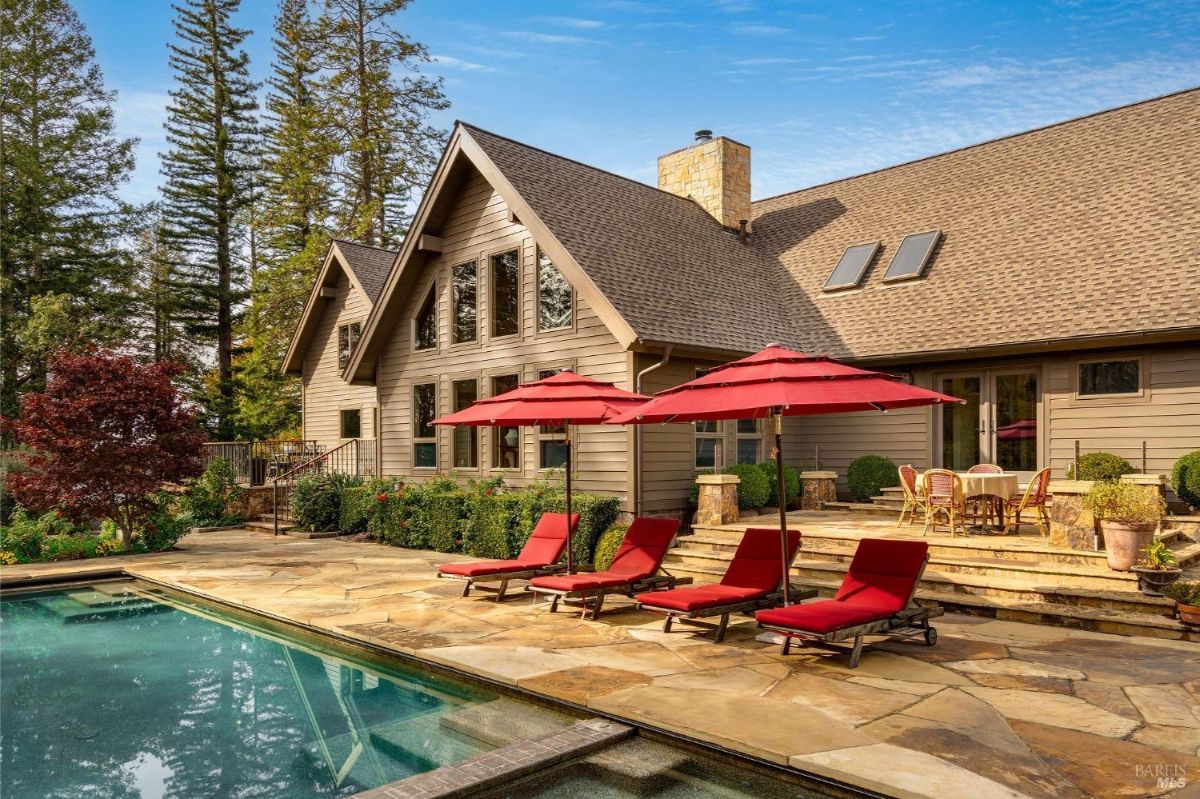 House with a large backyard featuring a swimming pool, patio, and red lounge chairs.