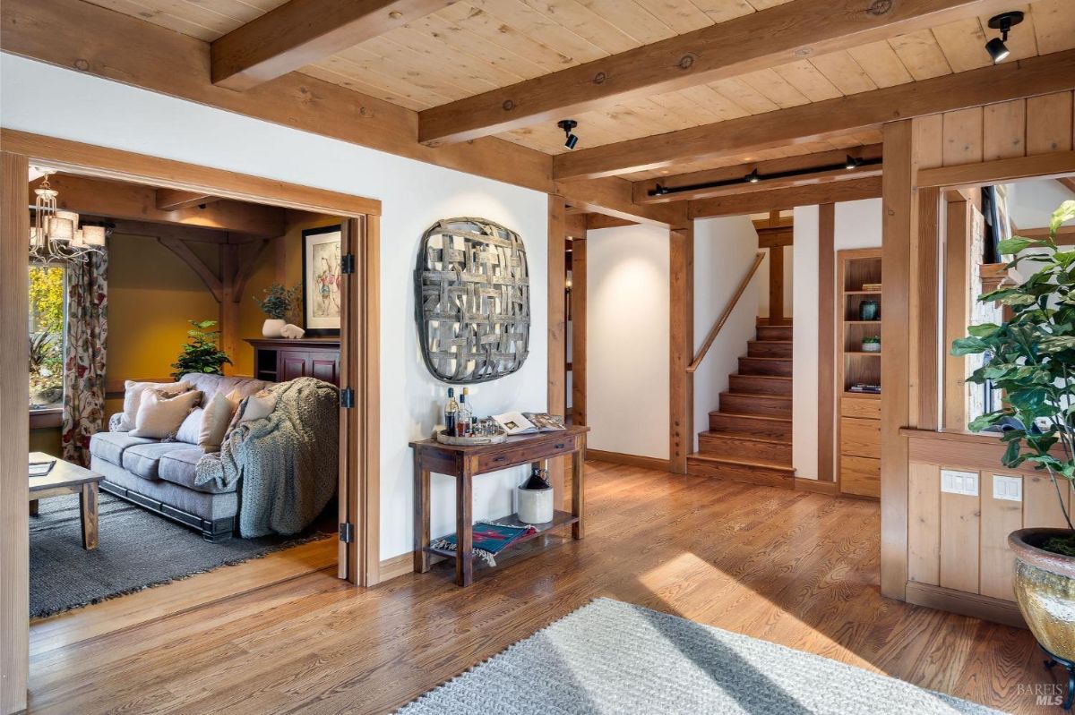 Entryway with wooden floors, beams, and a staircase leading to an upper level.