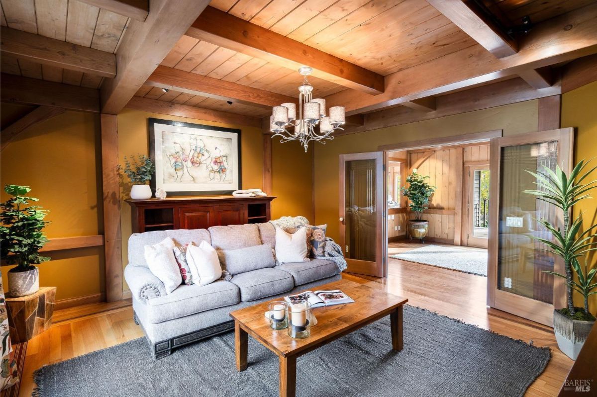 Small sitting room with a sofa, coffee table, and chandelier, decorated with warm tones and wood beams.