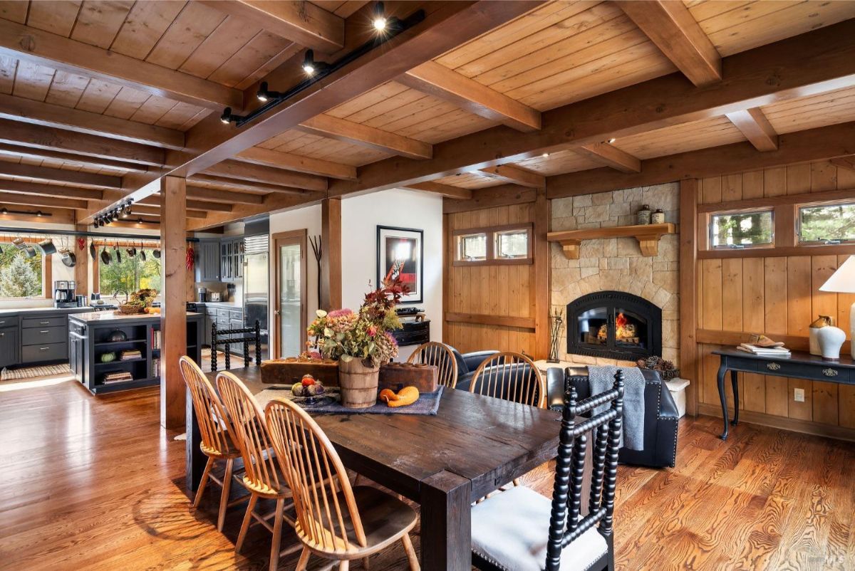 Open-concept space combines a dining area with a fireplace and a connected kitchen with wood beams and rustic decor.