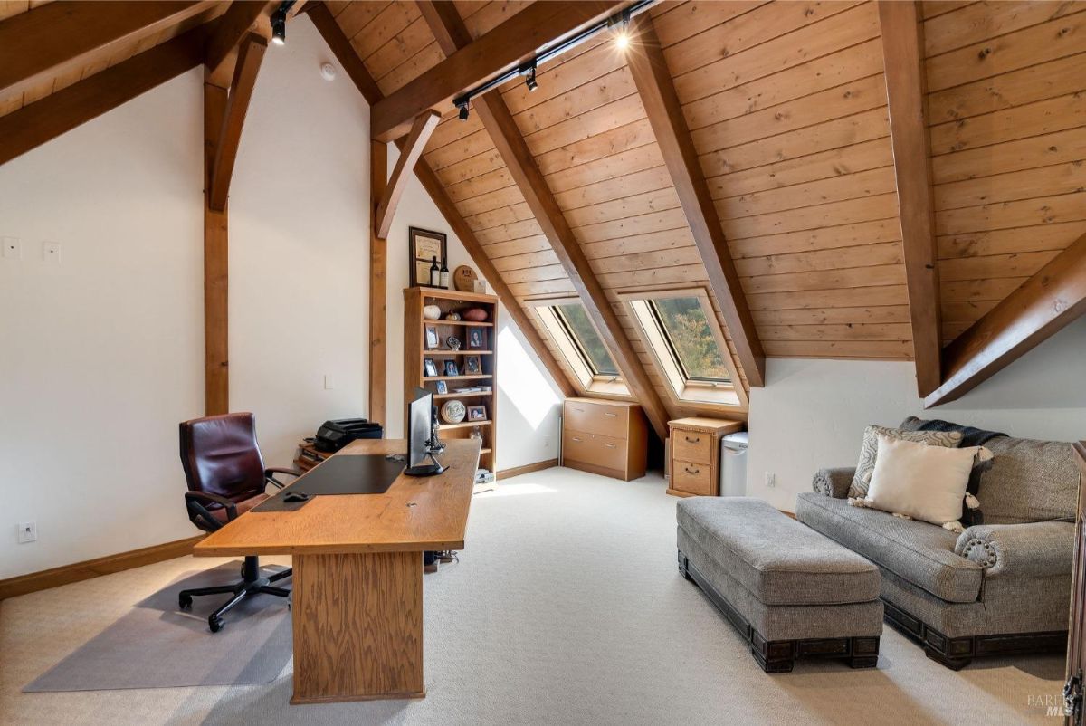 Home office space under a wooden vaulted ceiling with skylights, a desk, chair, and bookshelves.