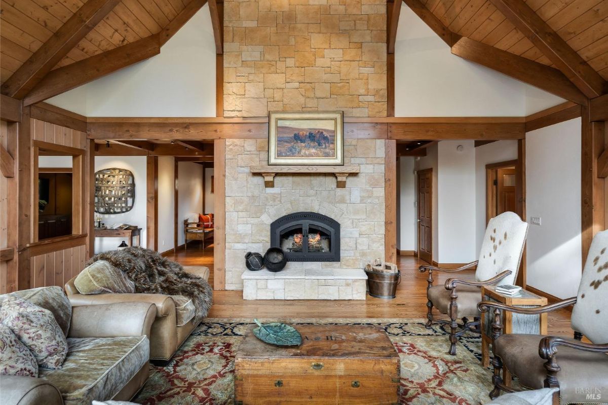 Living room featuring a stone fireplace with wooden mantle and exposed wood beams.