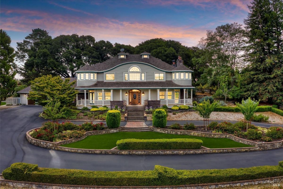 Two-story house with a wrap-around porch, a circular driveway, and a landscaped yard.