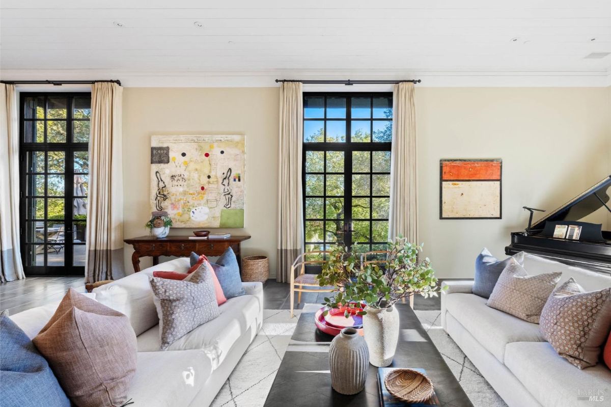 Living room with large windows, a grand piano, and colorful decor.