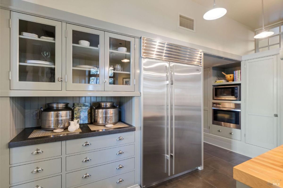 Kitchen view showing large stainless steel refrigerator, built-in microwave, and glass-front cabinetry.