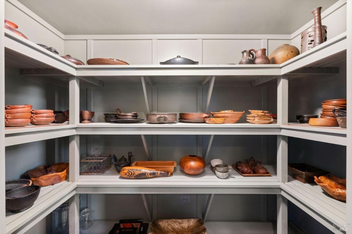 Pantry with multiple shelves holding wooden and ceramic dishes.