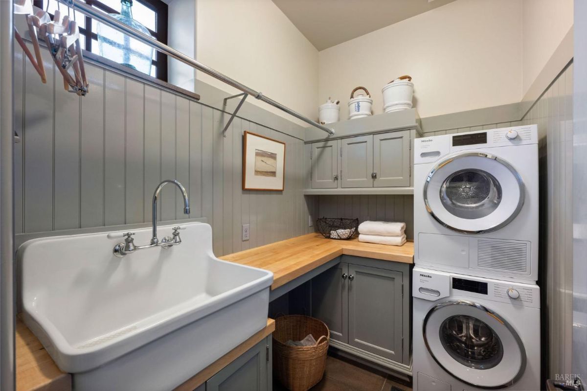 Laundry room with a farmhouse sink, stacked washer and dryer, and storage cabinets.