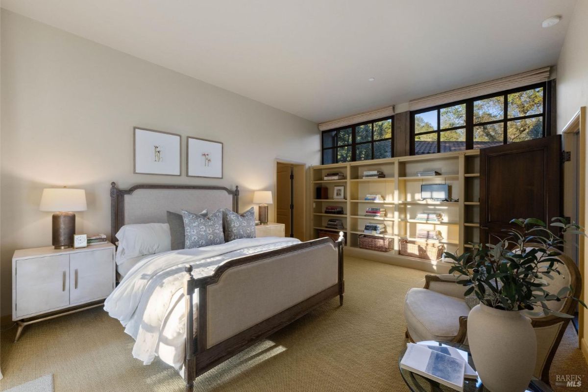 Bedroom featuring a large bed with a cushioned headboard, side tables, and bookshelves with storage bins against the wall.