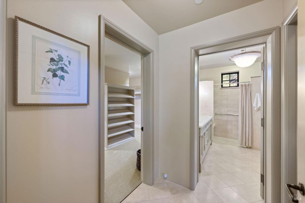 Hallway with a view of a closet and bathroom featuring simple beige walls and tiled floors.