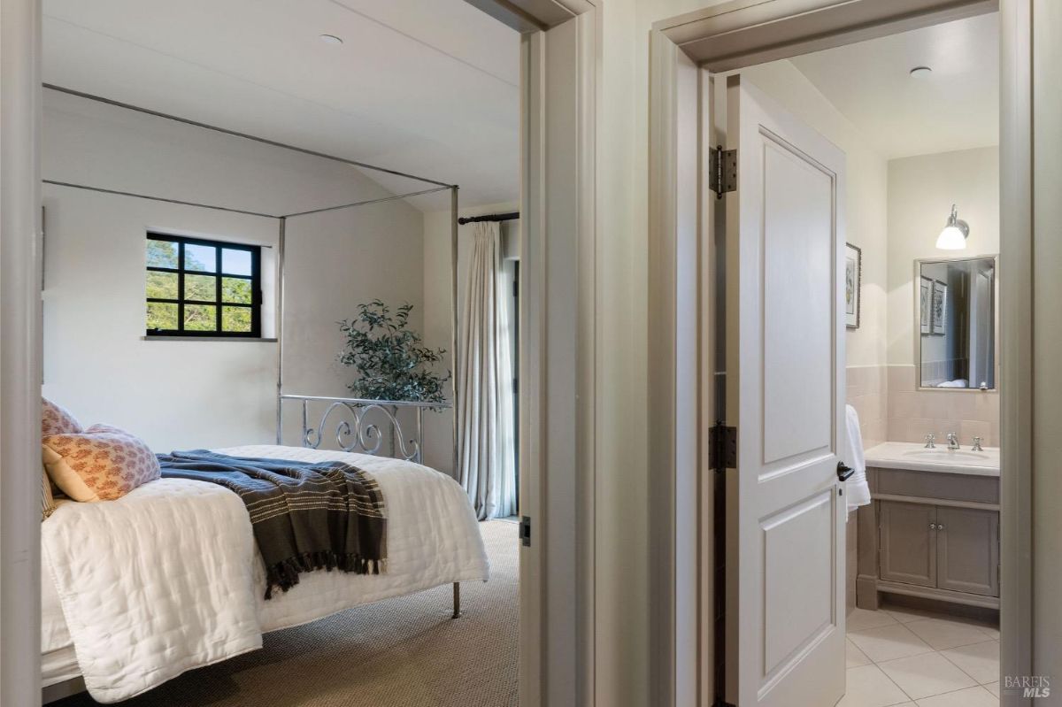 Bedroom with beige tones, a four-poster bed, and a small connected bathroom visible through an open door.