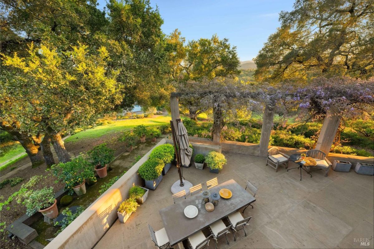 Outdoor dining area with a table and chairs surrounded by greenery and flowering plants.