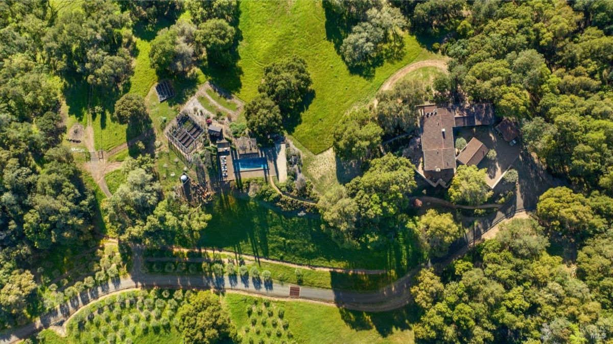 Aerial shot of a property showing a house, pool, and surrounding landscape.