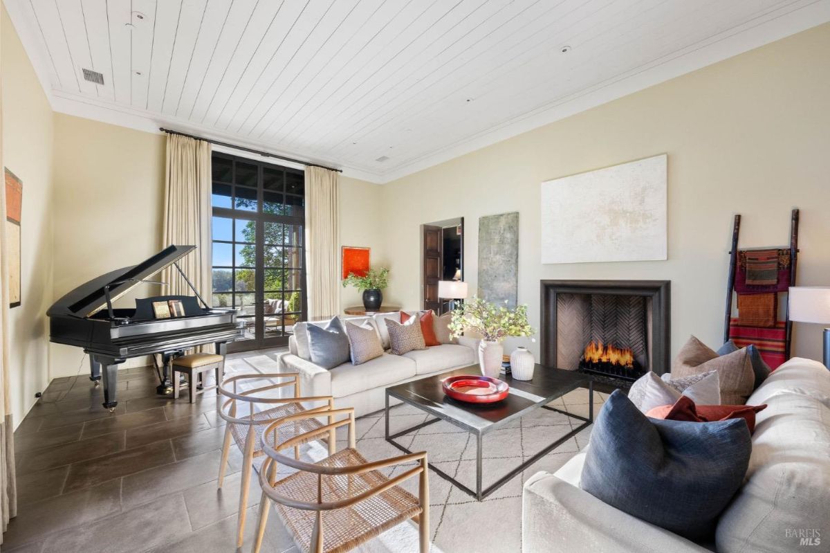 Living room with a grand piano, a fireplace, and large glass doors leading to a patio.