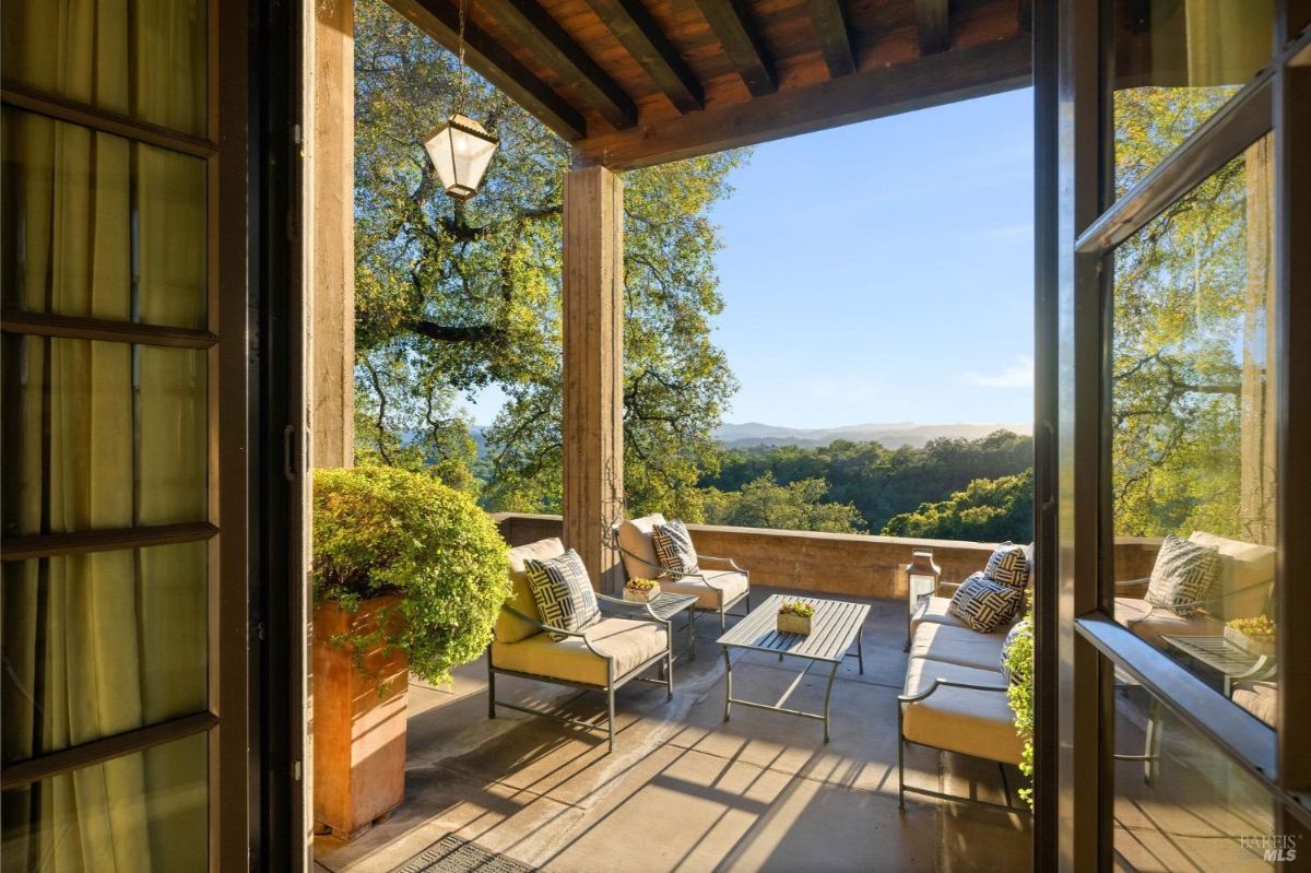 Balcony view shows a seating arrangement overlooking a tree-filled landscape and distant hills.