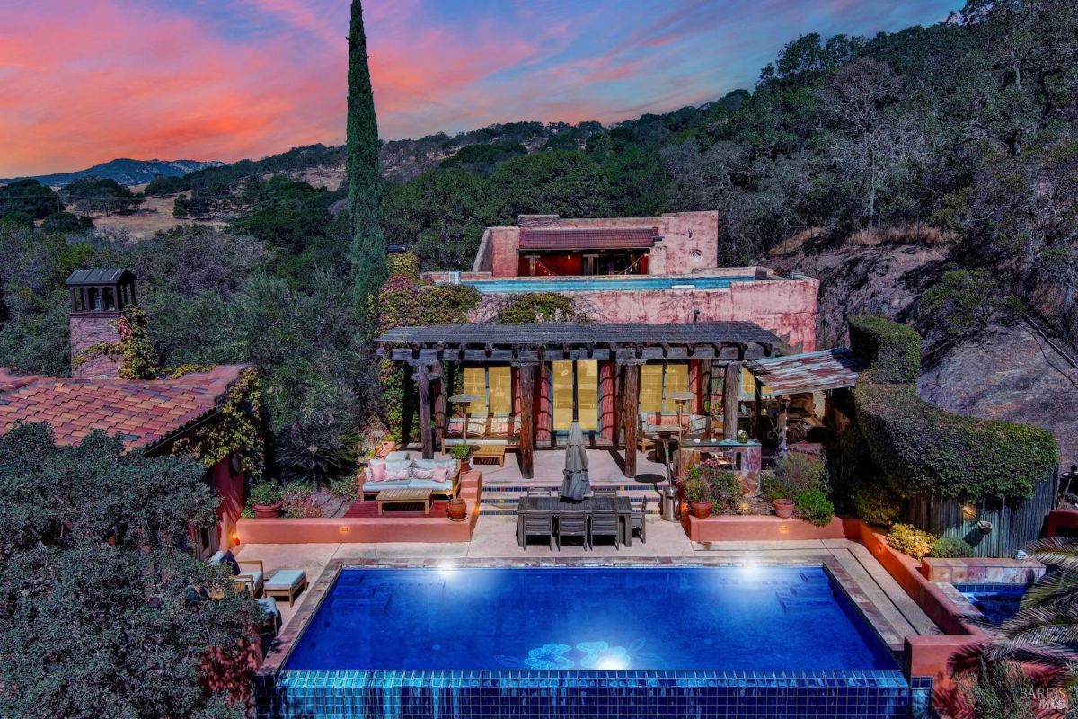 Poolside area with outdoor seating and a lush, green backdrop under a vibrant sunset.