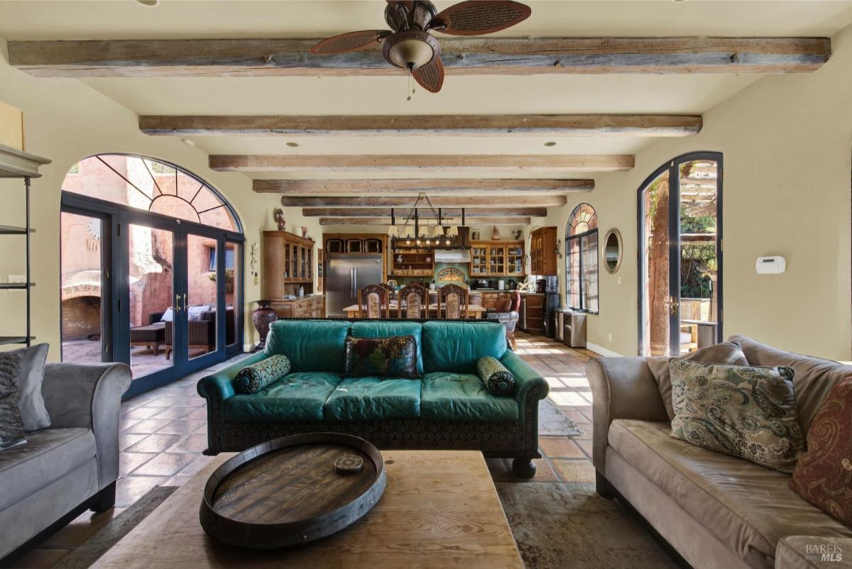 Open-concept living and dining area with exposed beams and bright, arched windows.