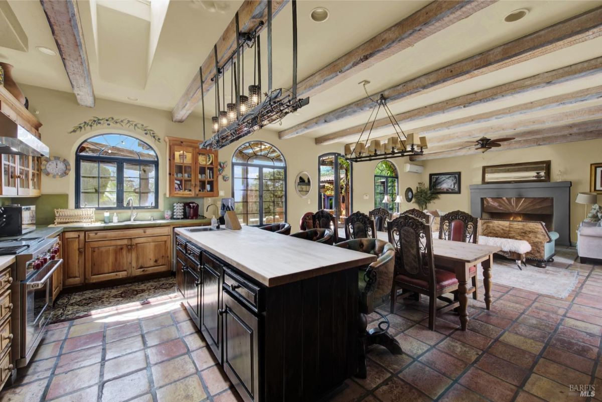 Kitchen features wooden cabinetry, a central island, and exposed ceiling beams with abundant natural light.