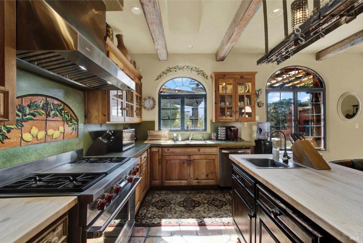 Decorative tile backsplash adds character to a fully-equipped kitchen with a professional stove and natural light from arched windows.