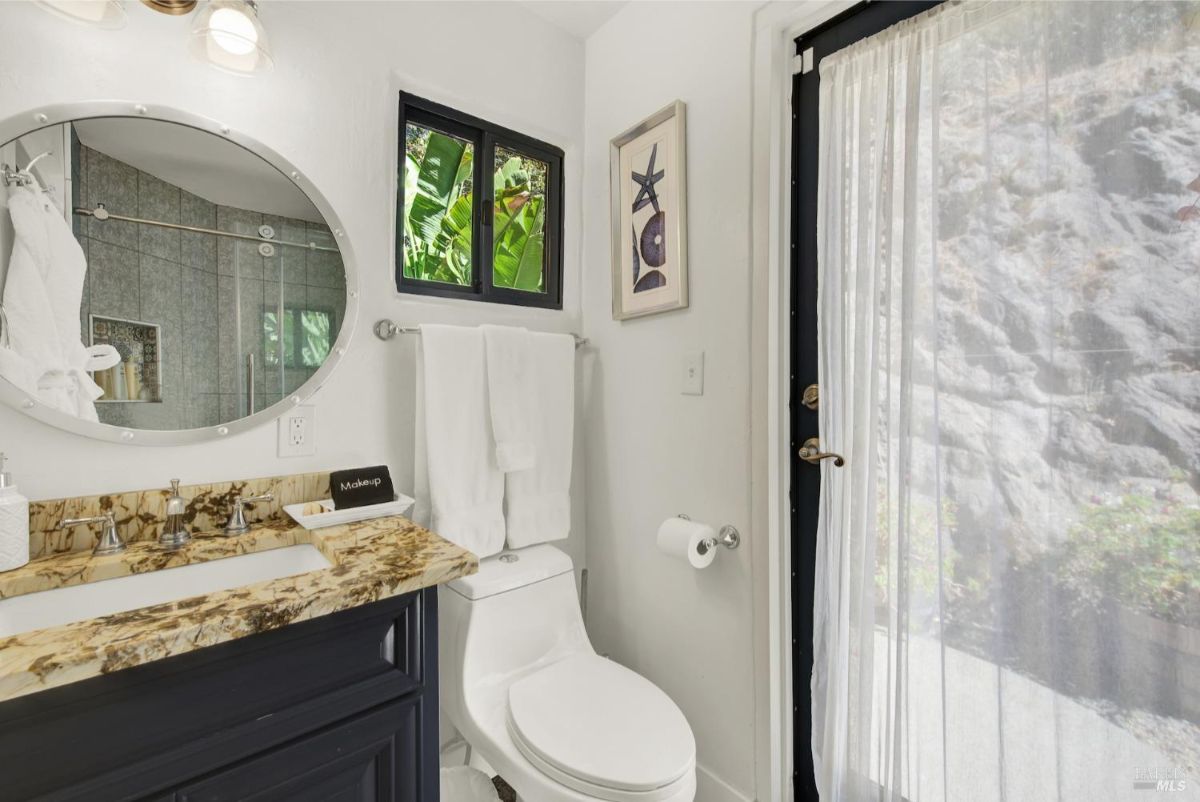 The bathroom has a sink, a toilet, a shower, and a door leading to the outdoors.