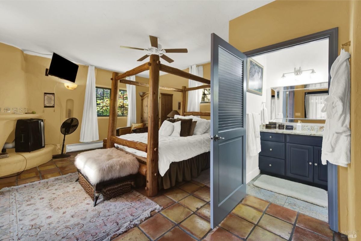 Room includes a rustic canopy bed, tiled flooring, and a cozy fireplace with a view into a modern bathroom.