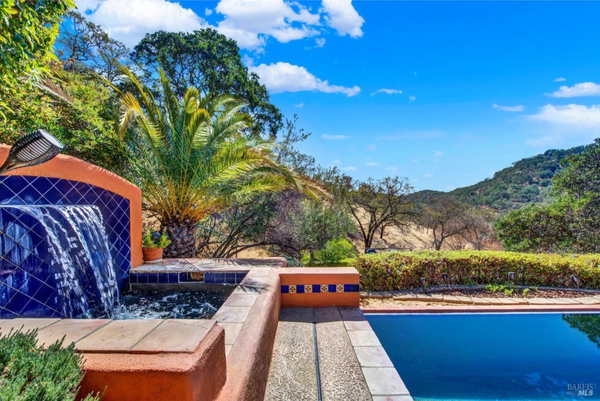 The pool area has a fountain, a palm tree, and a view of the hills.