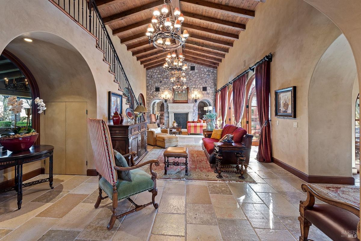  Interior perspective of the same living room, showing arched entryways, furniture arrangements, and a view of the fireplace. A staircase leads to a mezzanine level.