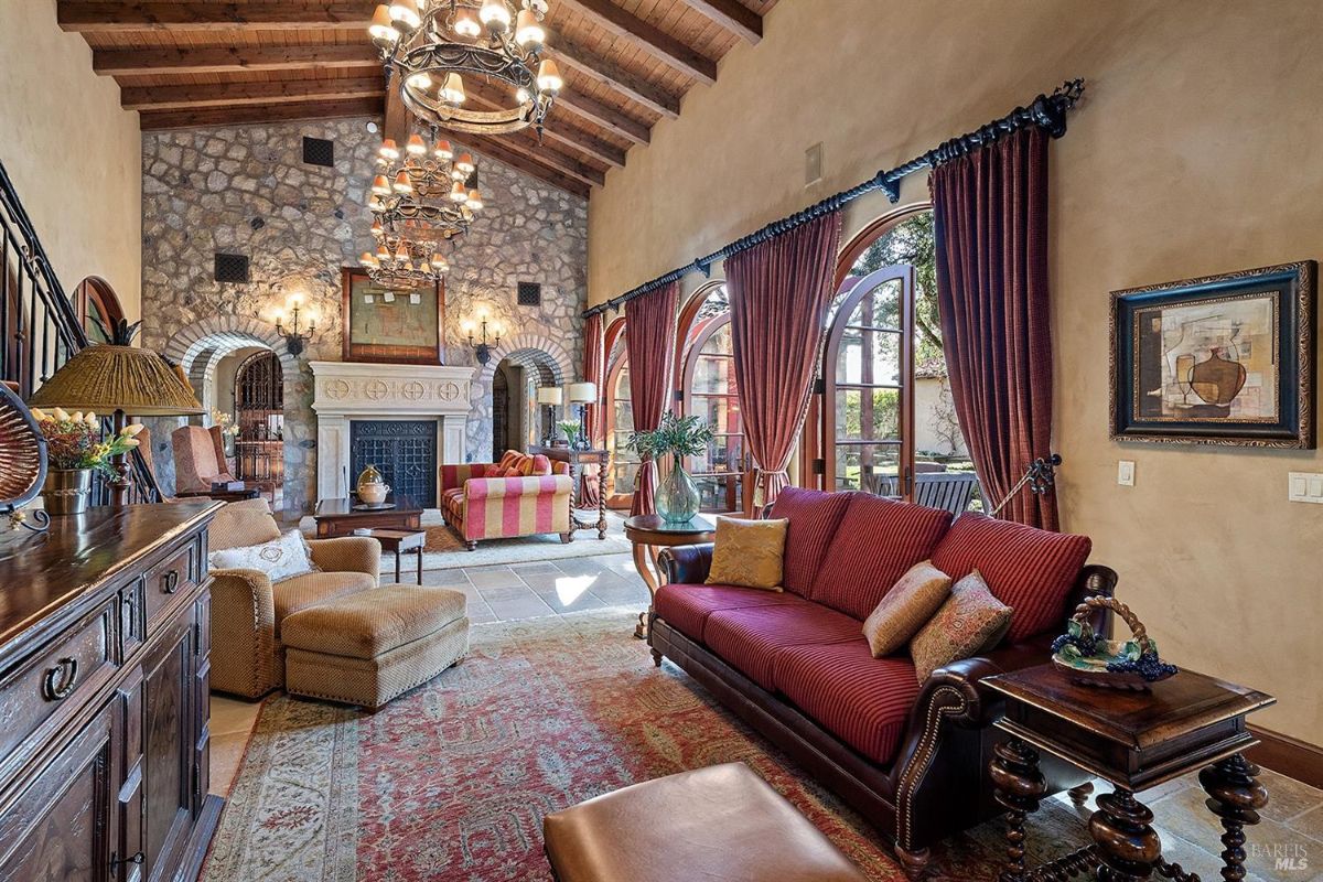 Focus on the seating area in front of the fireplace. The room includes patterned armchairs, a sofa, and a coffee table. There is visible stone wall architecture around the fireplace.