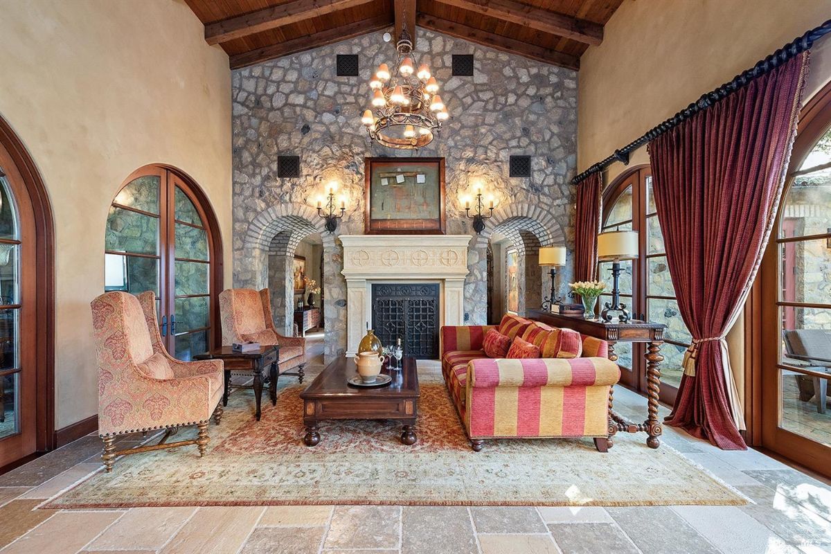 A closer view of the seating area in front of the fireplace, showing details of the furniture, the coffee table with decorative items, and the textured stone fireplace wall with sconces.