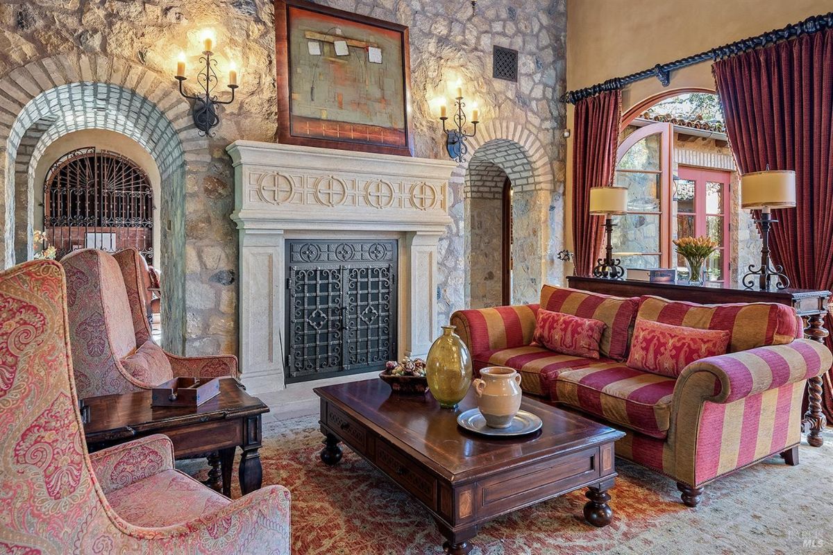 Another perspective of the main seating area, highlighting the coffee table, sofa, and armchairs. The arched windows open to an outdoor area, and decorative elements are placed throughout the room.