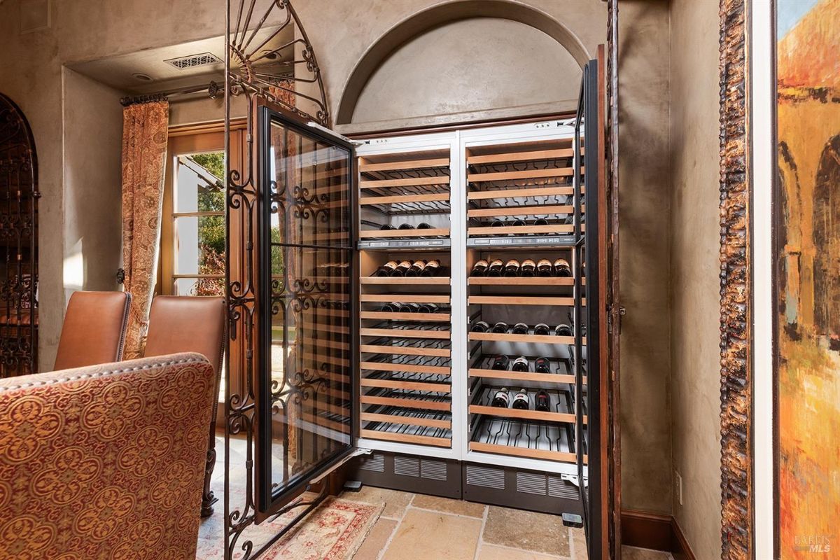 A wine cellar with wooden racks storing wine bottles. The racks are enclosed by a decorative iron gate.