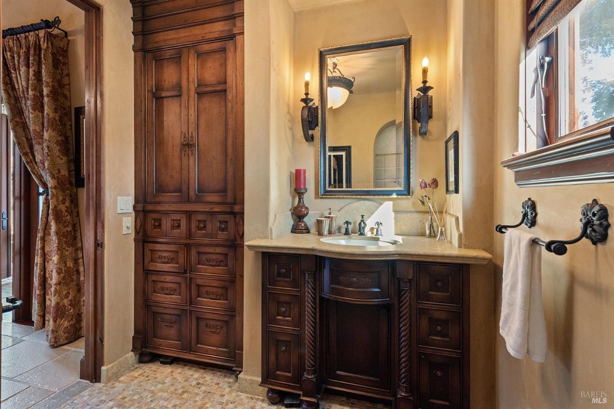 A bathroom with a wooden vanity, a sink, a mirror, and wall-mounted light fixtures. There is a cabinet for storage.