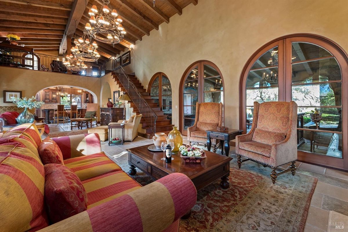 Interior perspective focusing on the room's wooden staircase, arched windows, and the open-plan layout. The seating includes upholstered chairs and sofas, with a clear view of the dining area.