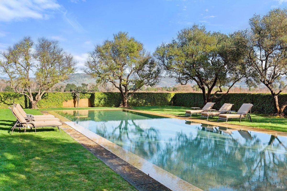 Swimming pool scene viewed from another angle, emphasizing the symmetry of the pool, the trees, and the hedges surrounding it.